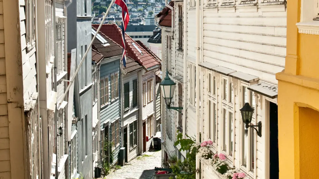 Characteristic steep alley in the historic neighbourhood of Bergen with Norwegian flag and shining sun.