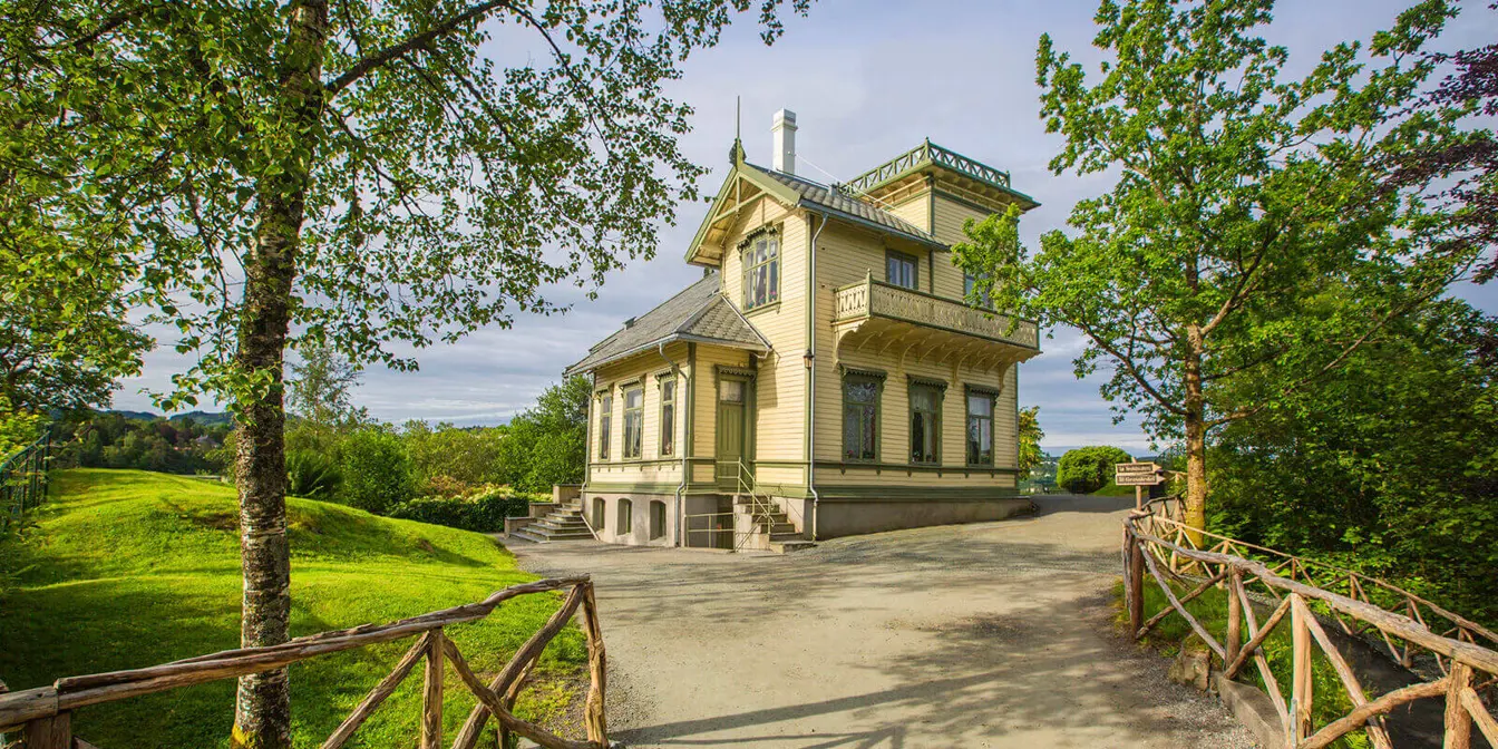 A large brick house on top of a small hill with green trees and plants around it.