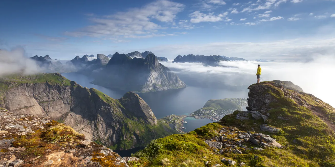 Man som står på en bergstopp i Lofoten och tittar ut över fjäll och hav.