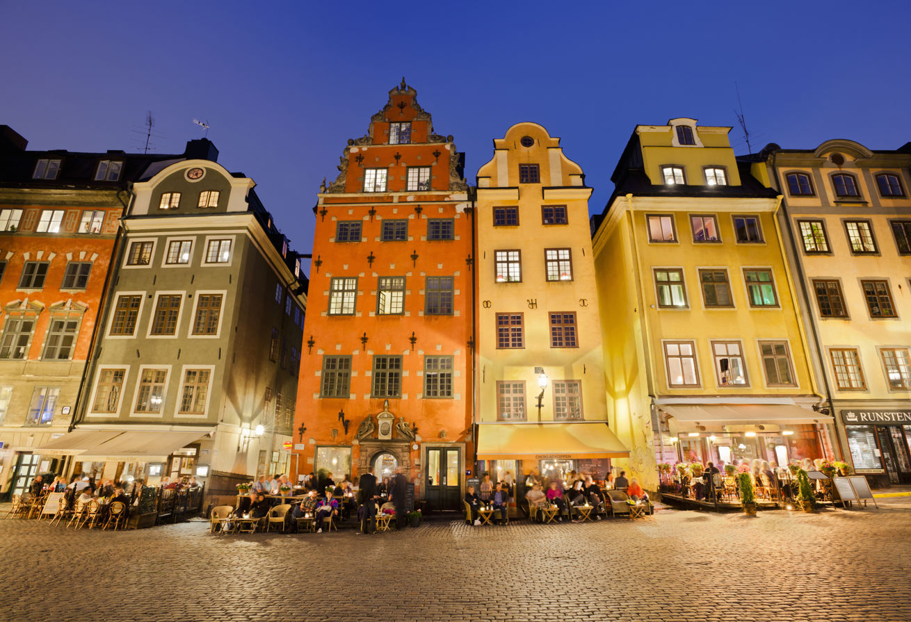 Bygninger i Gamla staden i Stockholm, sett forfra. Mennesker p&aring; uterestauranter foran bygningene. 