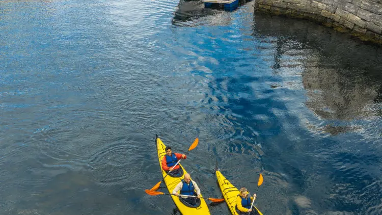 Two kayaks with four people in Brosundet paddling out of Ålesund city centre. Ålesund city centre in the background.